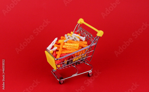 Multi-colored dowels in a miniature shopping cart on a red background