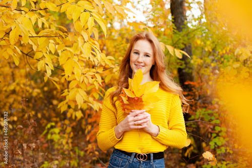 Autumn. red-haired girl in a yellow sweater holds a bouquet of autumn leaves in her hands. Warm tones. Orange. A place for text.
