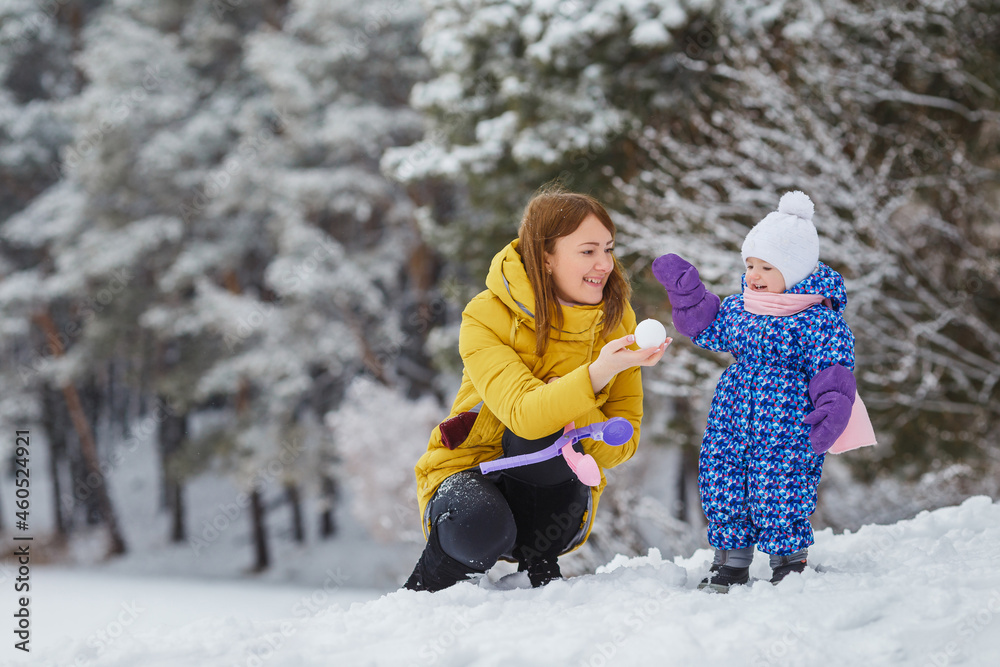 Young woman sculpt snowballs with her baby girl in the winter forest. Cute kid in warm clothes having fun outdoor with mother. Mom and daughter. Family holidays leisure, motherhood, love in family