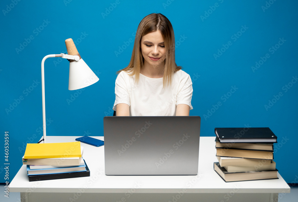 Portrait of a pretty young woman studying while sitting at the table with grey laptop computer, notebook. Smiling business woman working with a laptop isolated on a grey background. Portrait of a pretty young woman studying while sitting at the table with grey laptop computer, notebook. Smiling business woman working with a laptop isolated on a grey background.
