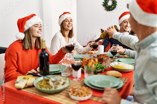 Group of young people smiling happy celebrating christmas drinking wine at home.
