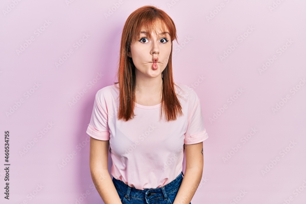 Redhead young woman wearing casual pink t shirt making fish face with lips, crazy and comical gesture. funny expression.