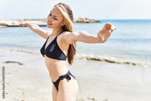 Young cuacasian girl wearing bikini breathing with arms open at the beach.