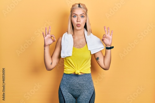 Beautiful blonde sports woman wearing workout outfit looking surprised and shocked doing ok approval symbol with fingers. crazy expression
