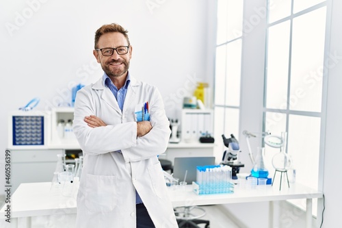 Middle age hispanic man wearing scientist uniform with arms crossed gesture at laboratory