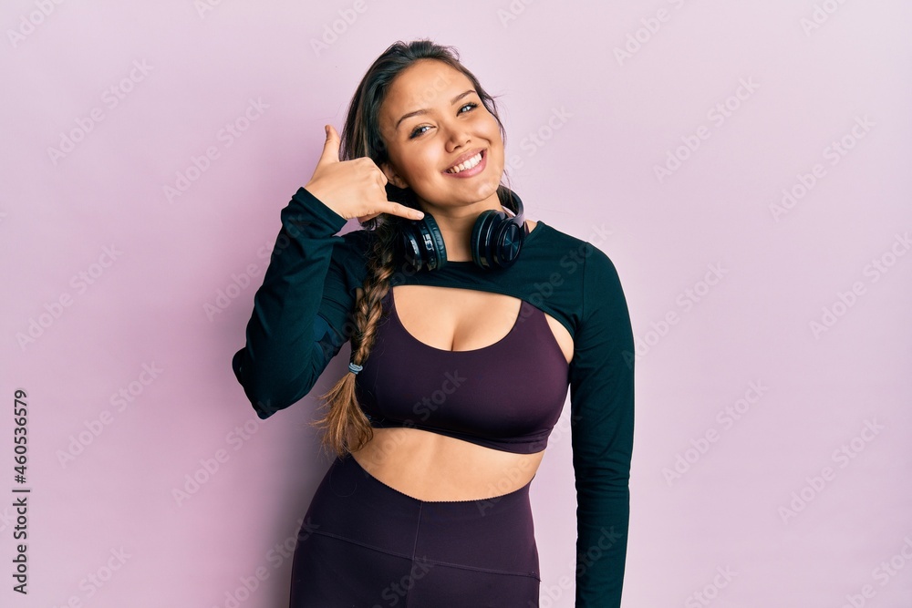 Young hispanic girl wearing sportswear and headphones smiling doing phone gesture with hand and fingers like talking on the telephone. communicating concepts.