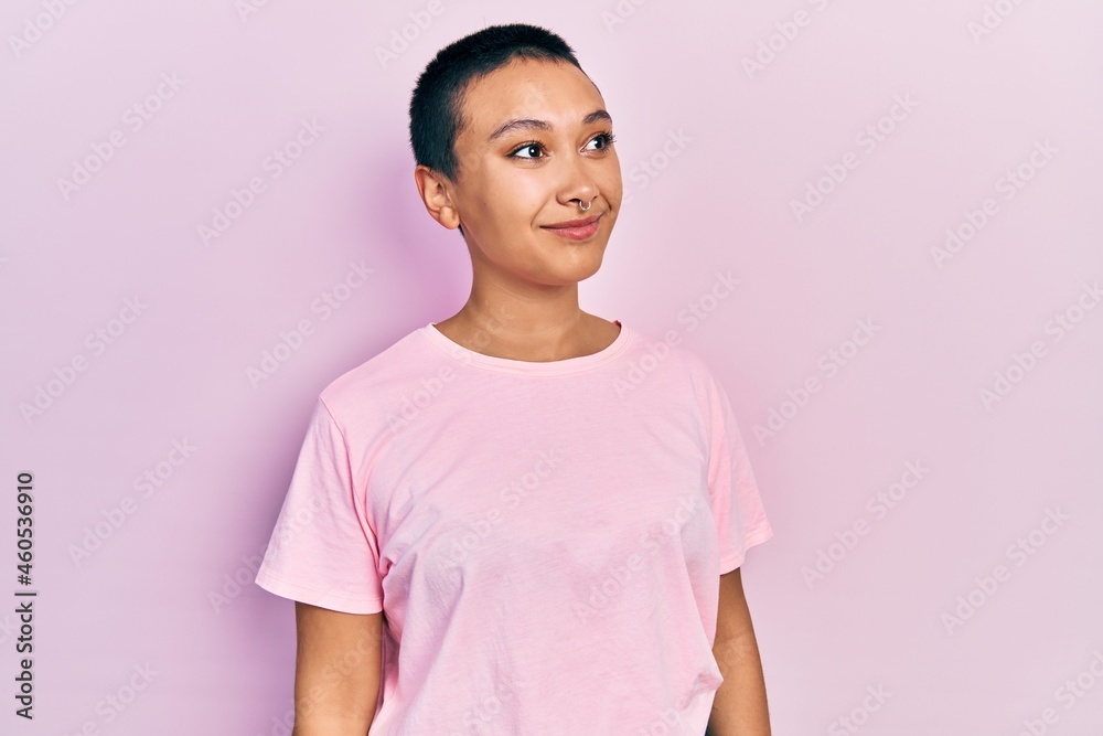 Beautiful hispanic woman with short hair wearing casual pink t shirt looking away to side with smile on face, natural expression. laughing confident. Beautiful hispanic woman with short hair wearing casual pink t shirt looking away to side with smile on face, natural expression. laughing confident.