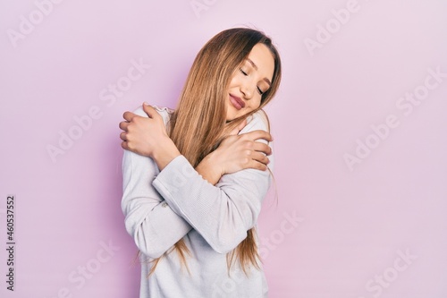 Young blonde girl wearing casual clothes hugging oneself happy and positive, smiling confident. self love and self care