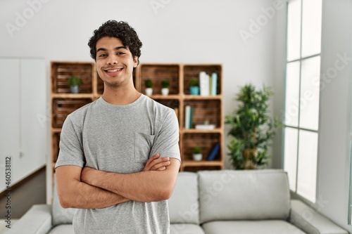 Young hispanic man smiling happy standing with arms crossed gesture at home.