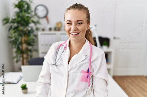 Young caucasian woman wearing doctor uniform and stethoscope at the clinic winking looking at the camera with sexy expression, cheerful and happy face.