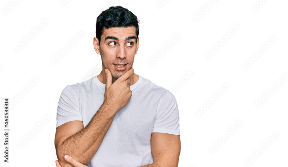 Handsome hispanic man wearing casual white t shirt with hand on chin thinking about question, pensive expression. smiling with thoughtful face. doubt concept.