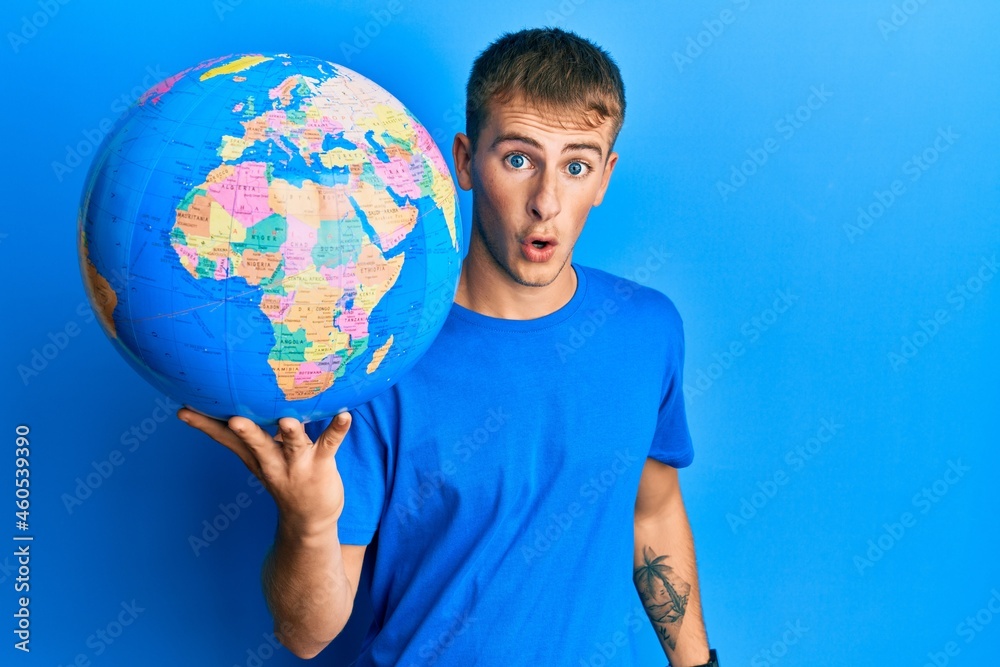 Young caucasian man holding world ball scared and amazed with open mouth for surprise, disbelief face Young caucasian man holding world ball scared and amazed with open mouth for surprise, disbelief face