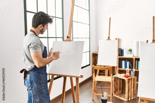 Young hispanic artist man smiling happy painting at art studio.