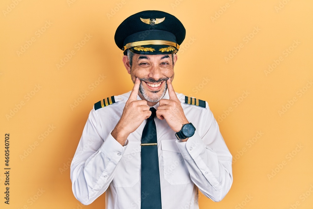 Handsome middle age man with grey hair wearing airplane pilot uniform smiling with open mouth, fingers pointing and forcing cheerful smile Handsome middle age man with grey hair wearing airplane pilot uniform smiling with open mouth, fingers pointing and forcing cheerful smile