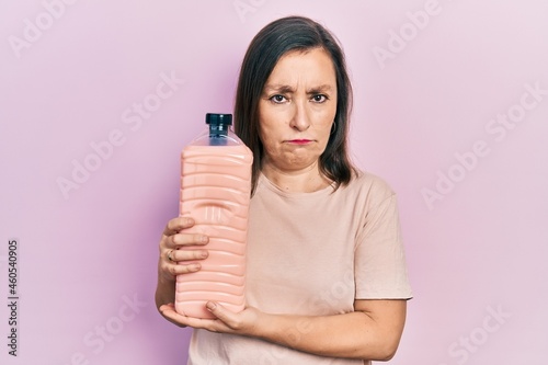 Middle age hispanic woman holding detergent bottle depressed and worry for distress, crying angry and afraid. sad expression.