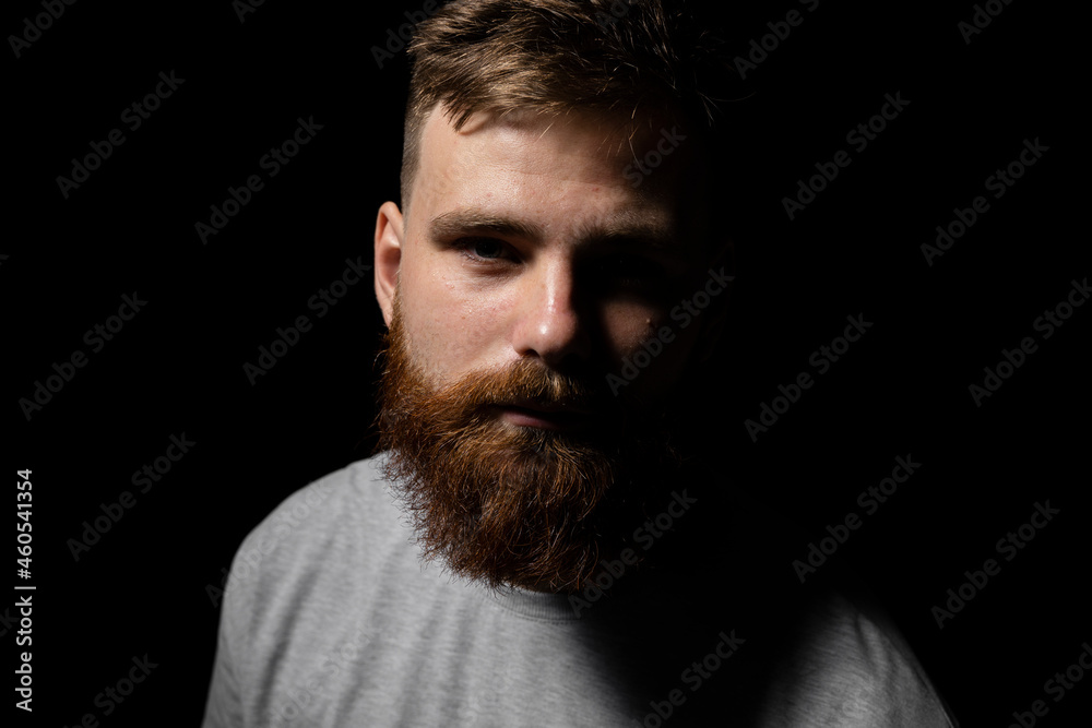 Fototapeta premium Close-up portrait of a handsome a brunette brutal bearded man in a grey t-shirt. Stylish and handsome man with a beard.