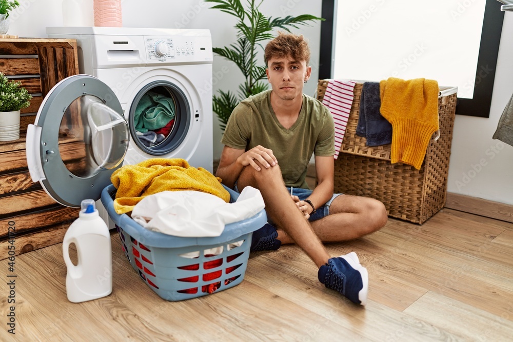 Young caucasian man putting dirty laundry into washing machine depressed and worry for distress, crying angry and afraid. sad expression. Young caucasian man putting dirty laundry into washing machine depressed and worry for distress, crying angry and afraid. sad expression.