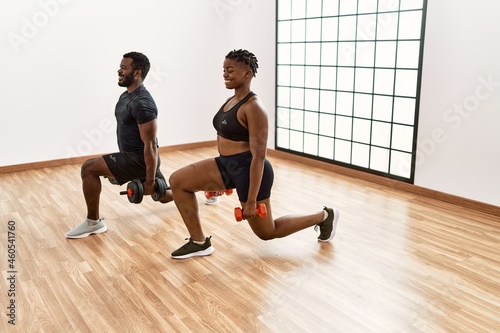 Young african american sporty couple training power exercise using dumbbells at sport center.
