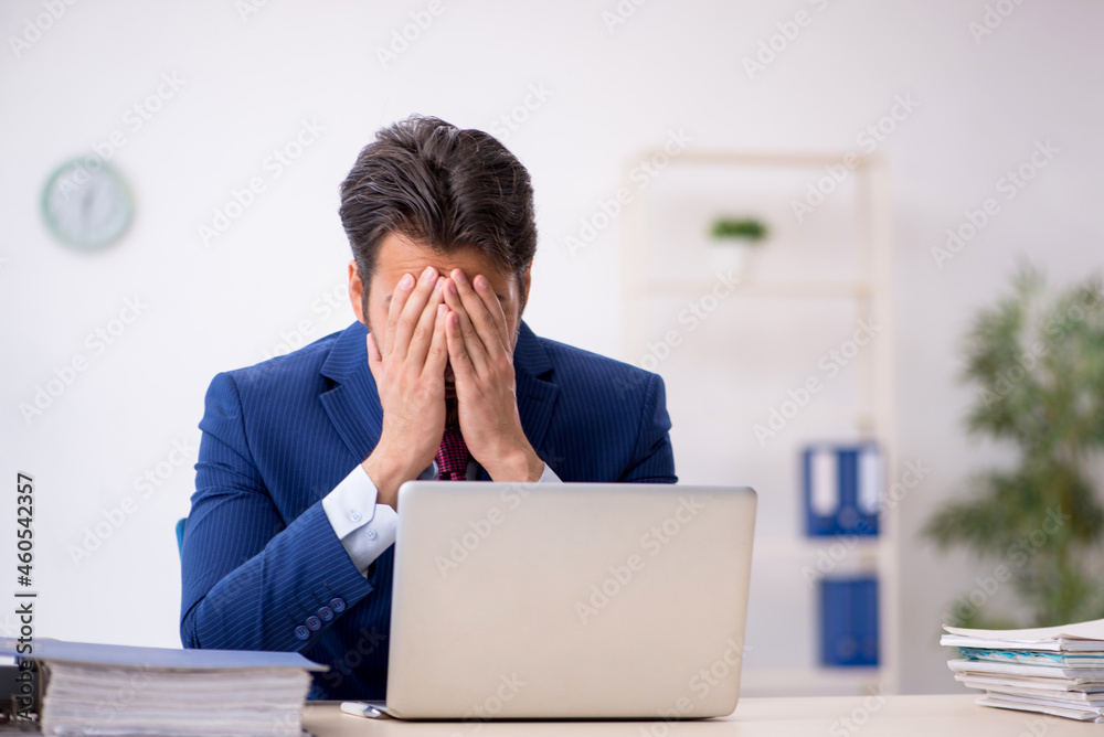 Young male employee unhappy with excessive work in the office Young male employee unhappy with excessive work in the office