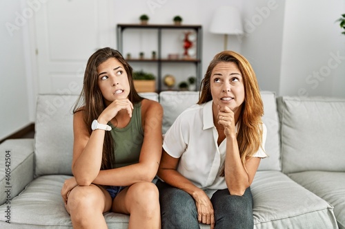 Mother and daughter together sitting on the sofa at home thinking worried about a question, concerned and nervous with hand on chin