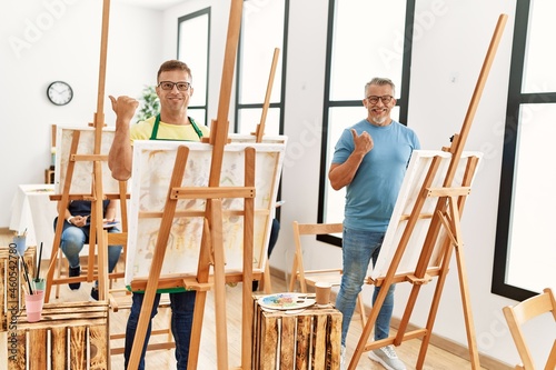 Group of middle age people artist at art studio pointing thumb up to the side smiling happy with open mouth