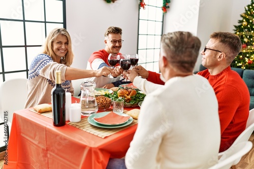 Group of middle age people smiling happy having christmas dinner toasting with wine at home.
