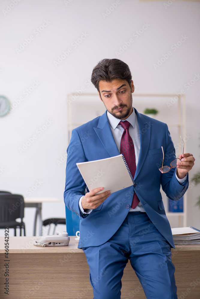 Young male employee reading paper at workplace