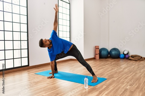 Handsome hispanic man doing exercise and stretching on yoga mat, practicing flexibility and training at the gym