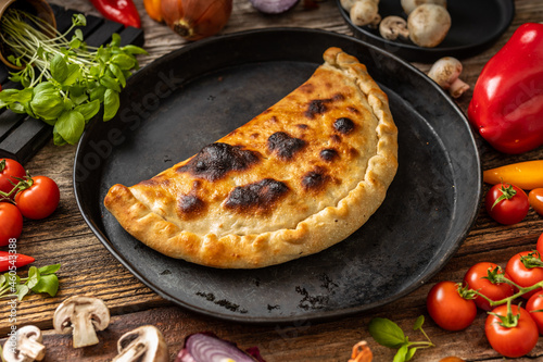 Pizza calzone on a black plate with vegetables