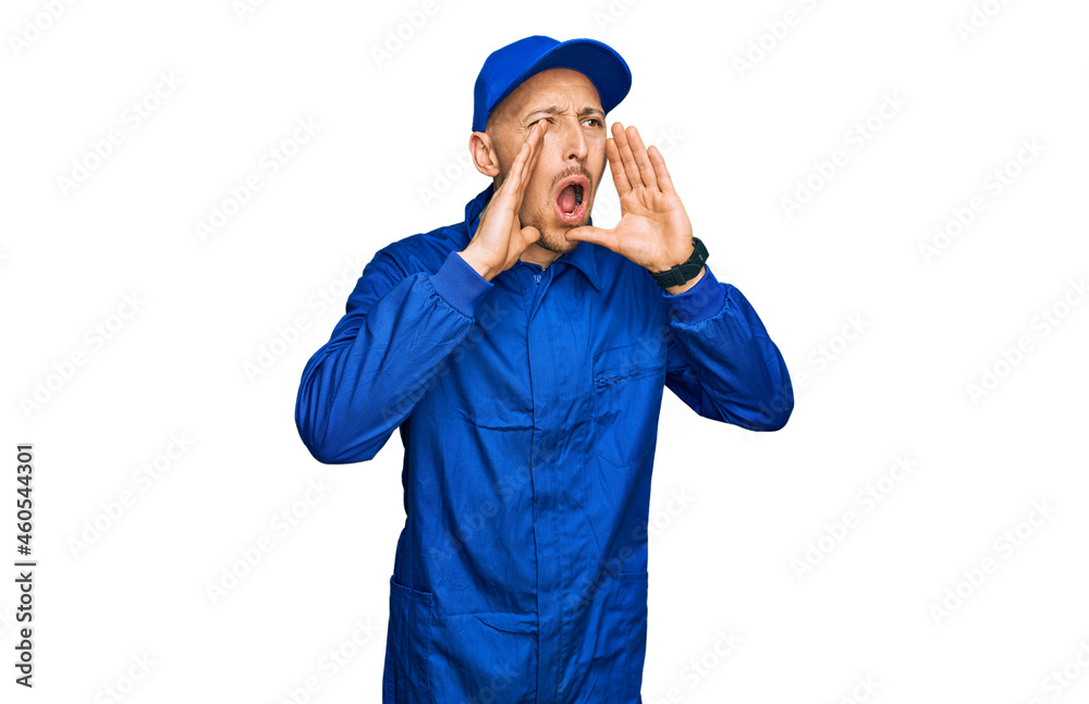 Bald man with beard wearing builder jumpsuit uniform shouting angry out loud with hands over mouth Bald man with beard wearing builder jumpsuit uniform shouting angry out loud with hands over mouth