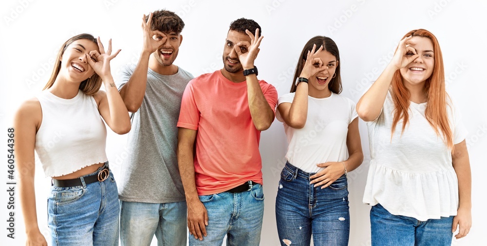 Group of young friends standing together over isolated background doing ok gesture with hand smiling, eye looking through fingers with happy face. Group of young friends standing together over isolated background doing ok gesture with hand smiling, eye looking through fingers with happy face.