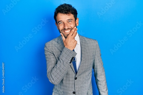 Handsome man with beard wearing business suit and tie looking confident at the camera smiling with crossed arms and hand raised on chin. thinking positive.