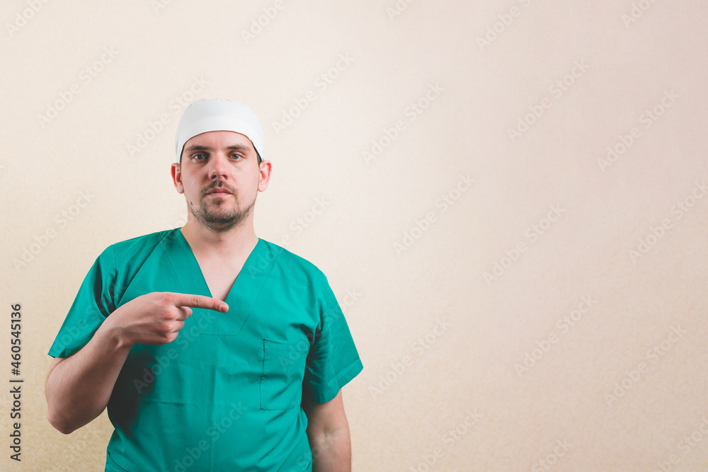 Young doctor in green suit pointing his fingers right into copyspace isolated