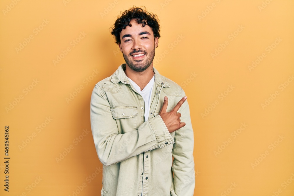 Young hispanic man wearing casual clothes cheerful with a smile of face pointing with hand and finger up to the side with happy and natural expression on face