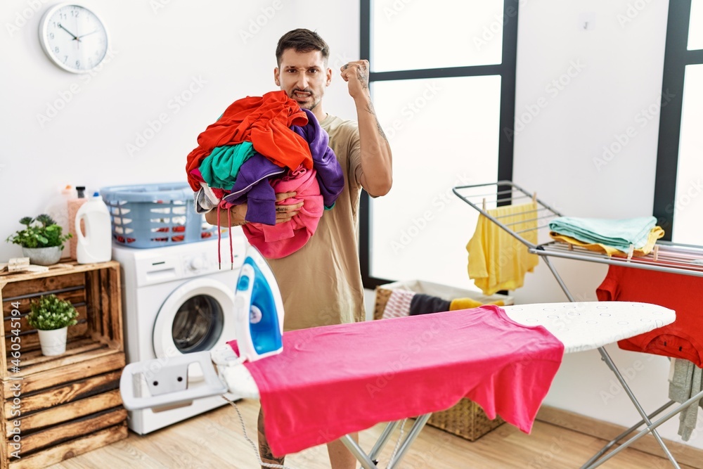 Young handsome man holding laundry ready to iron annoyed and frustrated shouting with anger, yelling crazy with anger and hand raised Young handsome man holding laundry ready to iron annoyed and frustrated shouting with anger, yelling crazy with anger and hand raised