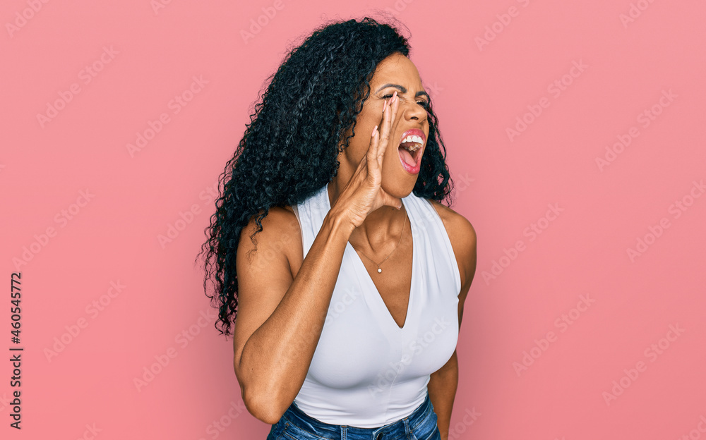 Middle age african american woman wearing casual style with sleeveless shirt shouting and screaming loud to side with hand on mouth. communication concept. Middle age african american woman wearing casual style with sleeveless shirt shouting and screaming loud to side with hand on mouth. communication concept.