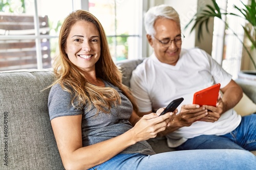 Middle age hispanic couple smiling happy using tablet and smartphone at home.