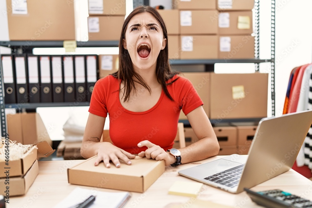 Young hispanic woman preparing order working at storehouse angry and mad screaming frustrated and furious, shouting with anger. rage and aggressive concept. Young hispanic woman preparing order working at storehouse angry and mad screaming frustrated and furious, shouting with anger. rage and aggressive concept.