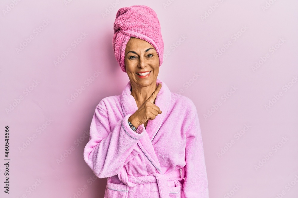 Middle age hispanic woman wearing shower towel cap and bathrobe with a big smile on face, pointing with hand and finger to the side looking at the camera. Middle age hispanic woman wearing shower towel cap and bathrobe with a big smile on face, pointing with hand and finger to the side looking at the camera.