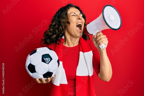 Middle age hispanic woman hooligan screaming through megaphone supporting soccer team photo