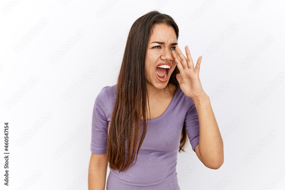 Young brunette woman standing by isolated background shouting and screaming loud to side with hand on mouth. communication concept. Young brunette woman standing by isolated background shouting and screaming loud to side with hand on mouth. communication concept.
