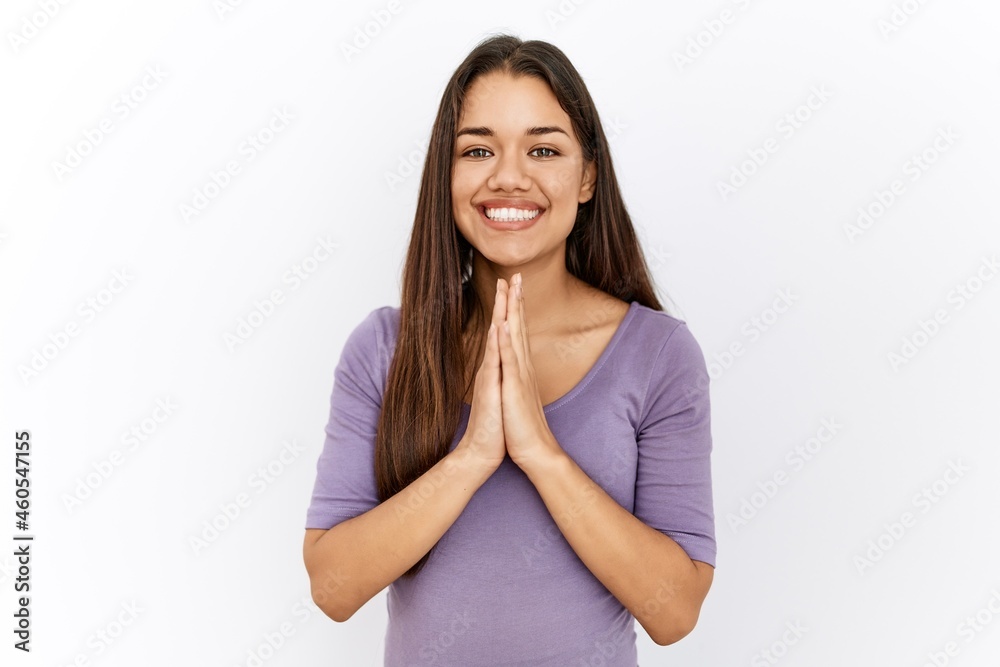 Young brunette woman standing by isolated background praying with hands together asking for forgiveness smiling confident. Young brunette woman standing by isolated background praying with hands together asking for forgiveness smiling confident.