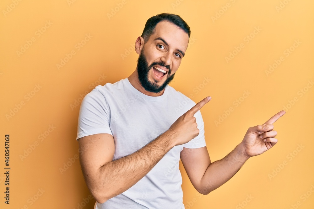 Young man with beard wearing casual white t shirt smiling and looking at the camera pointing with two hands and fingers to the side. Young man with beard wearing casual white t shirt smiling and looking at the camera pointing with two hands and fingers to the side.