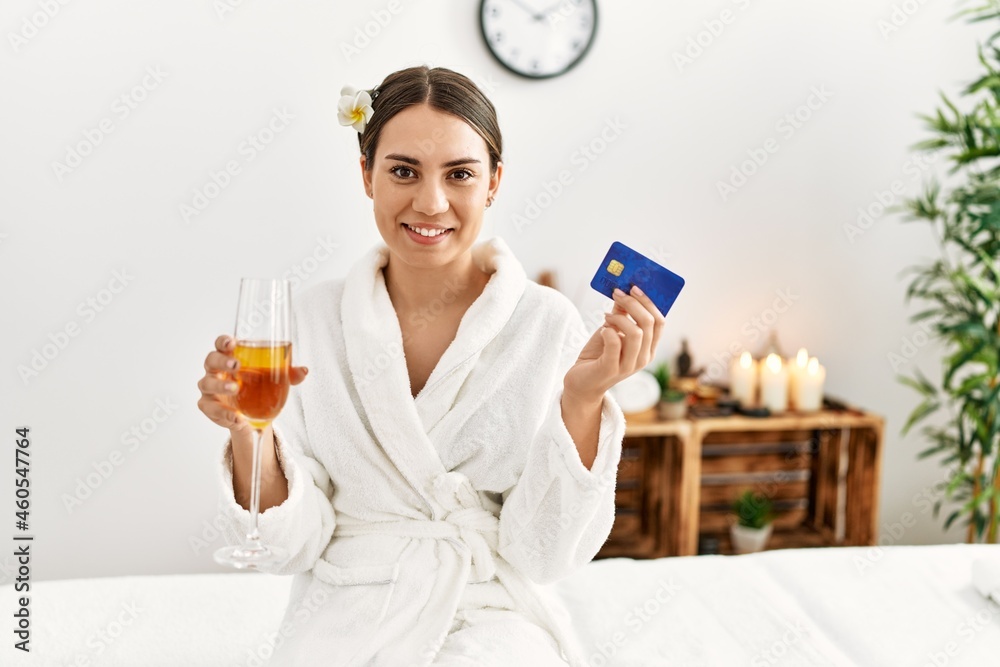 Young hispanic woman holding credit card drinking champagne at beauty center. Young hispanic woman holding credit card drinking champagne at beauty center.