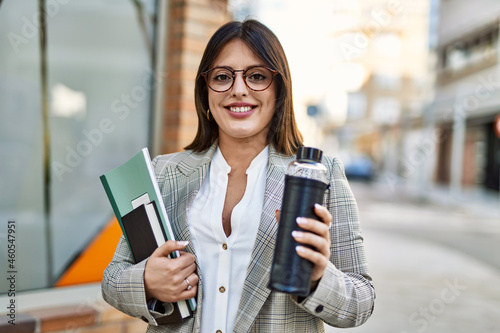 Young hispanic businesswoman smiling happy holding bottle of water at the city.