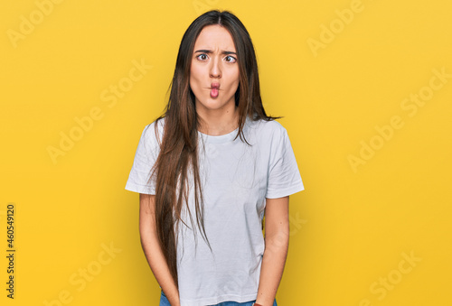 Young hispanic girl wearing casual white t shirt making fish face with lips, crazy and comical gesture. funny expression.