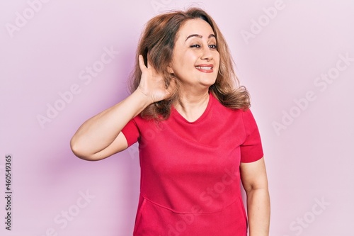 Middle age caucasian woman wearing casual clothes smiling with hand over ear listening an hearing to rumor or gossip. deafness concept.
