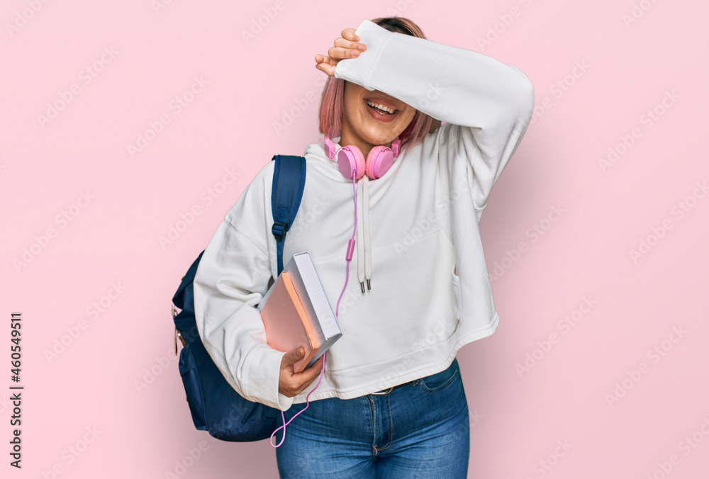 Hispanic woman with pink hair wearing student backpack and headphones smiling cheerful playing peek a boo with hands showing face. surprised and exited Hispanic woman with pink hair wearing student backpack and headphones smiling cheerful playing peek a boo with hands showing face. surprised and exited
