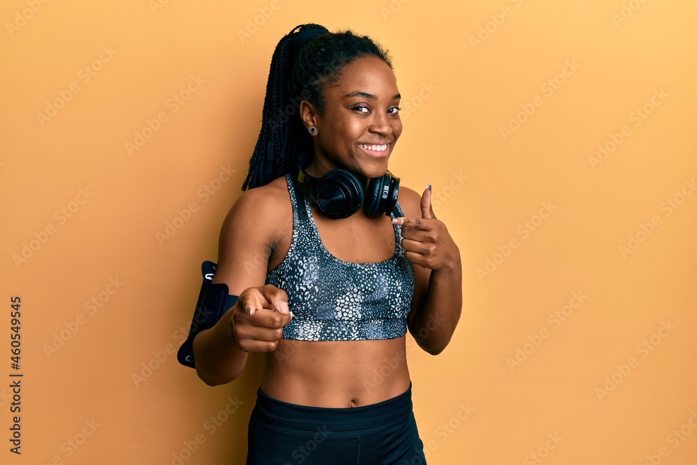 African american woman with braided hair wearing sportswear and arm band pointing fingers to camera with happy and funny face. good energy and vibes. African american woman with braided hair wearing sportswear and arm band pointing fingers to camera with happy and funny face. good energy and vibes.