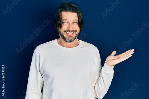 Middle age caucasian man wearing casual clothes smiling cheerful presenting and pointing with palm of hand looking at the camera.